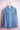 Light blue denim jacket with long sleeves and buttoned pockets hanging on wooden hanger