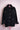 Black corduroy jacket with front buttons and lace-trimmed chest pockets on a pink mannequin