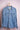 Light blue denim shirt with buttoned chest pockets hanging on wooden hanger against pink wall