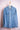 Light blue denim men's shirt with buttoned chest pockets hanging on wooden hanger