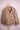 Beige casual jacket with front pockets hanging on wooden hanger against pink background