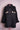Black denim jacket with floral embroidery on chest pockets displayed on pink hanger against light pink background