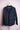 Dark blue casual jacket with front pockets hanging on wooden hanger against pink background