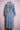 Long denim trench coat with embroidered lion design in brown, white, and red on back against pink background