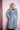 Smiling woman wearing light blue denim trench coat with belt against pale pink background