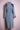 Back view of long denim trench coat with black beaded shoulder embellishments on pink background