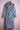 Light blue denim trench coat with double-breasted buttons and black beaded shoulder embellishments on pink dress form