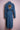 Back view of long blue denim trench coat with tiger face embroidery and belt on pink mannequin